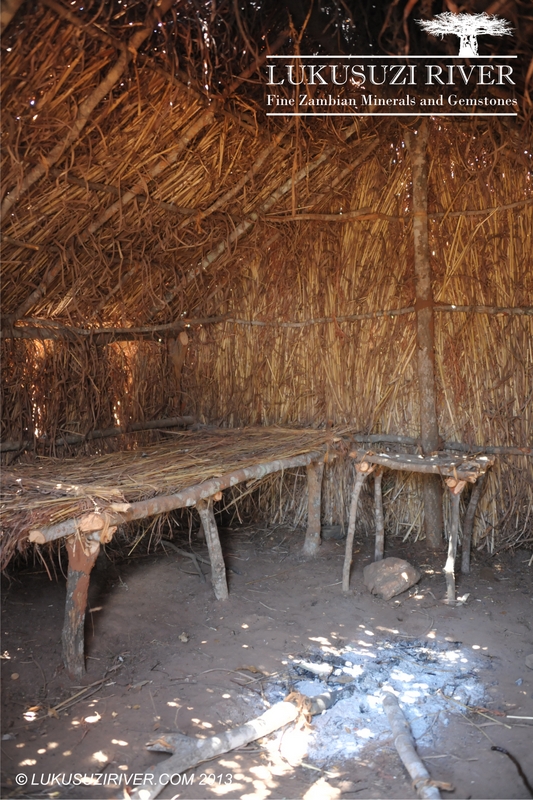 Zumwanda: A bed, a bedside table and a camp fire inside a straw house.
